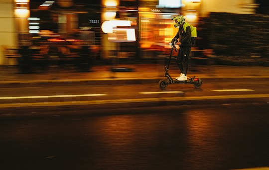 Persona en patinete eléctrico de noche sobre calle mojada